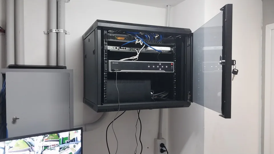 Rack de networking instalado en gabinete de pared, con monitor de cámaras a la vista